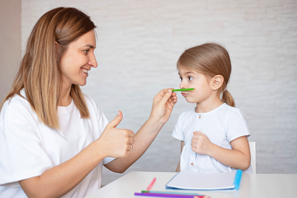 a speech language pathologist wearing a white shirt teaches facial motor skills to a young girl